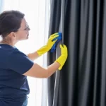 Fotografía de una mujer que sabe cómo lavar cortinas de blackout limpiando con delicadeza las cortinas